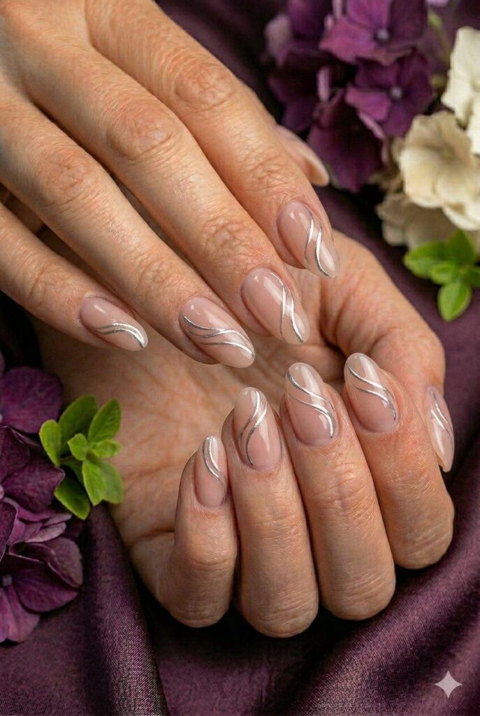 Soft nude prom nails with metallic silver swirl lines for a graceful formal design