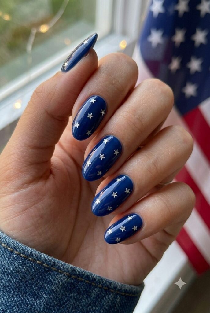 Short almond nails with deep blue polish and tiny silver star glitter