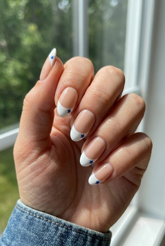 Short almond nails with nude base bright white French tips and tiny blue star accents