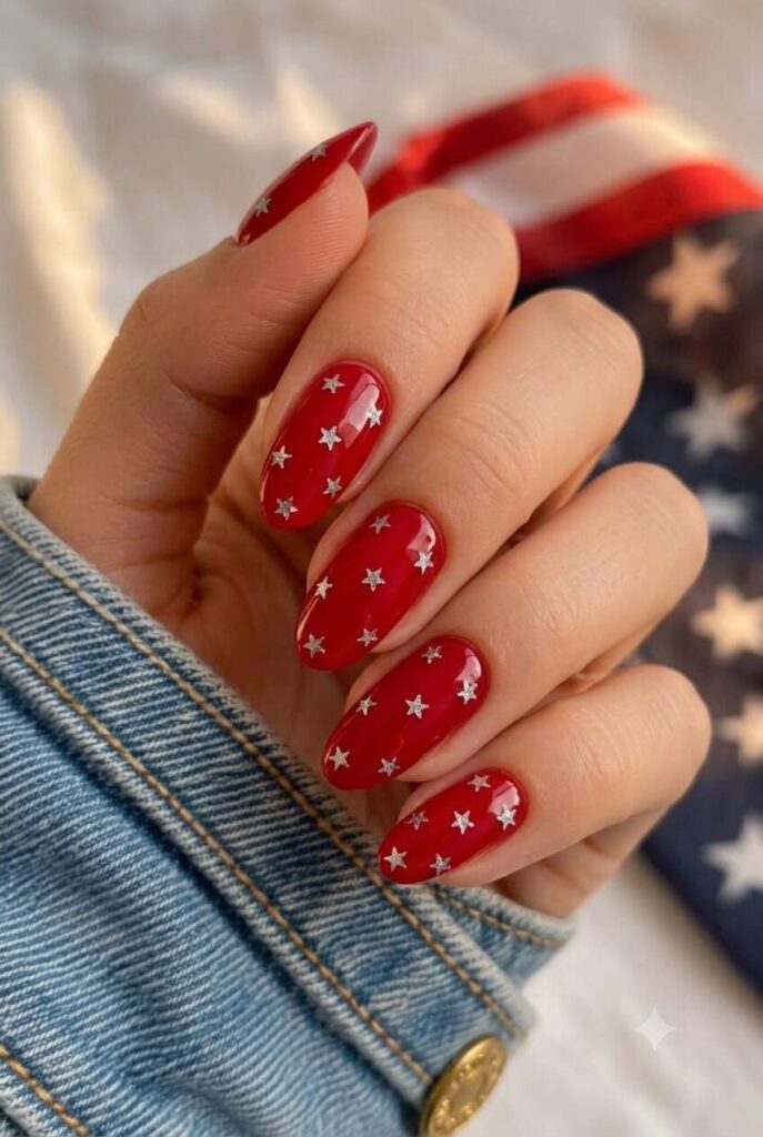 Short almond nails with red polish and tiny silver star glitter accents