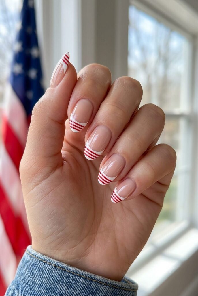 Short almond nails with nude base white French tips and tiny red stripe details