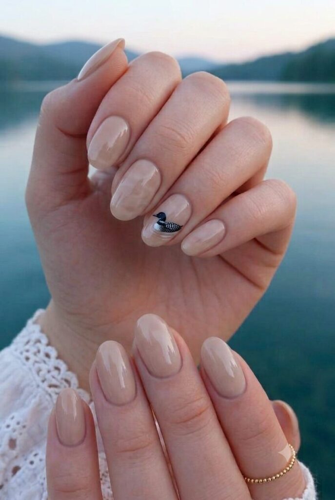 Short almond nails with nude base and tiny black white loon accent