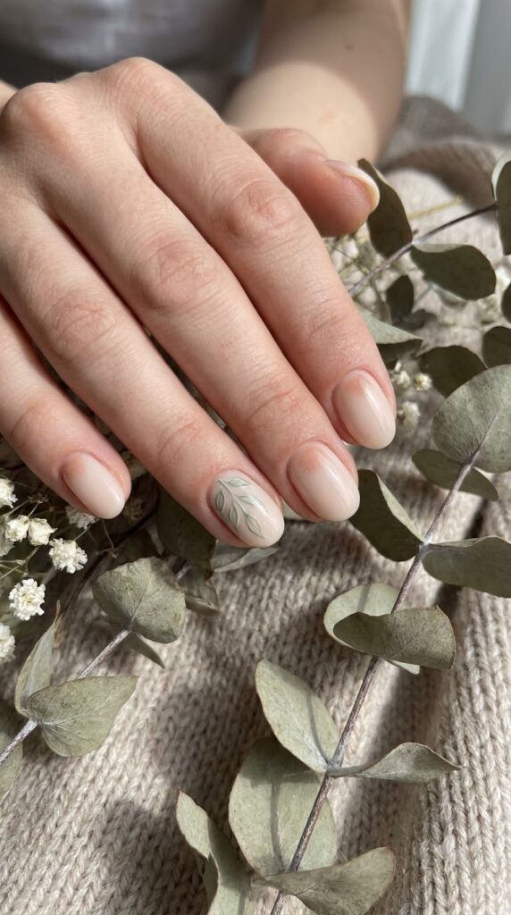 Short oval nails with nude base, dusty peach, and sage leaf art