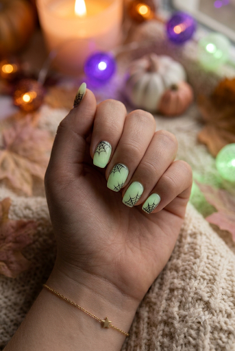 Almond nails with pale green glow polish and fine black spider webs