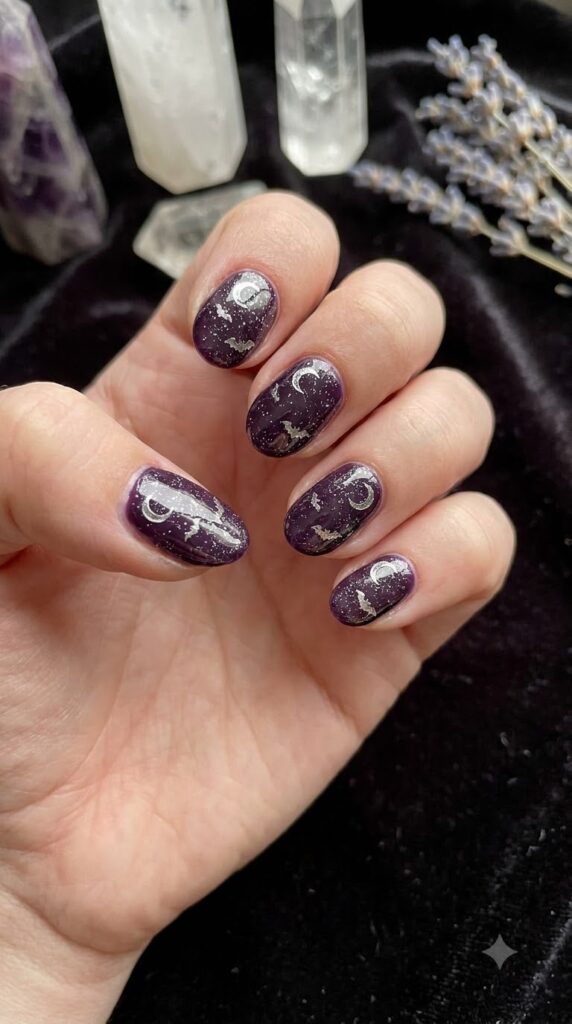 Short oval nails in deep witchy purple with silver moon and bat accents