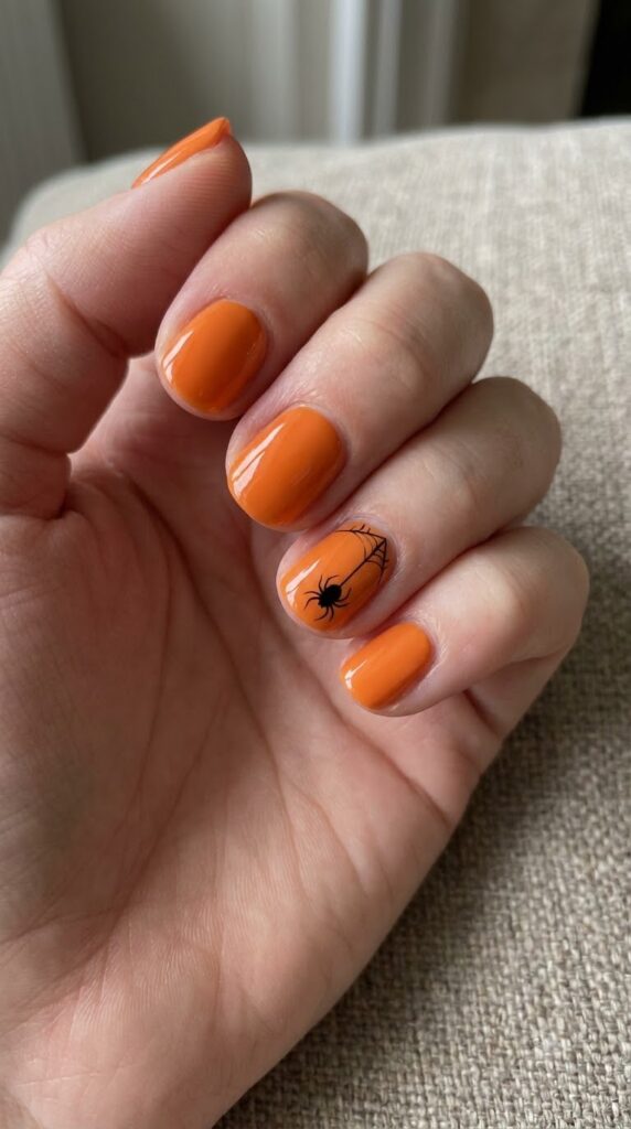 Short orange nails with a single black hanging spider accent