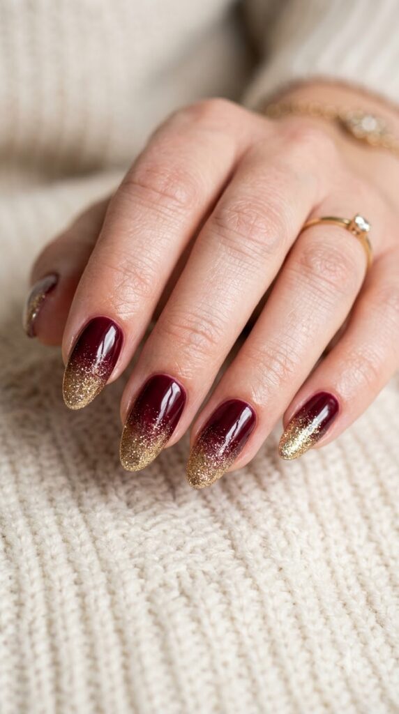 Almond burgundy wine nails blending into fine metallic gold glitter tips