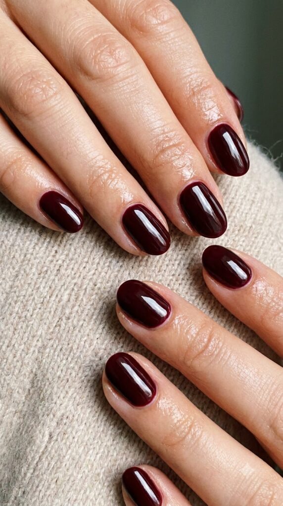 Short oval nails painted in opaque deep burgundy wine glossy polish