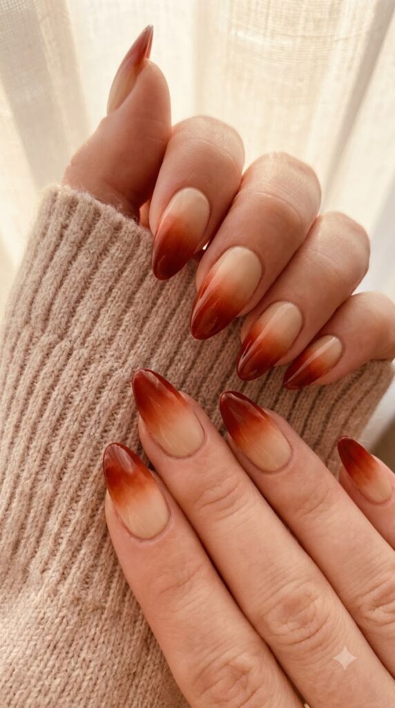 Almond nails with nude base fading smoothly into deep burnt amber red tips