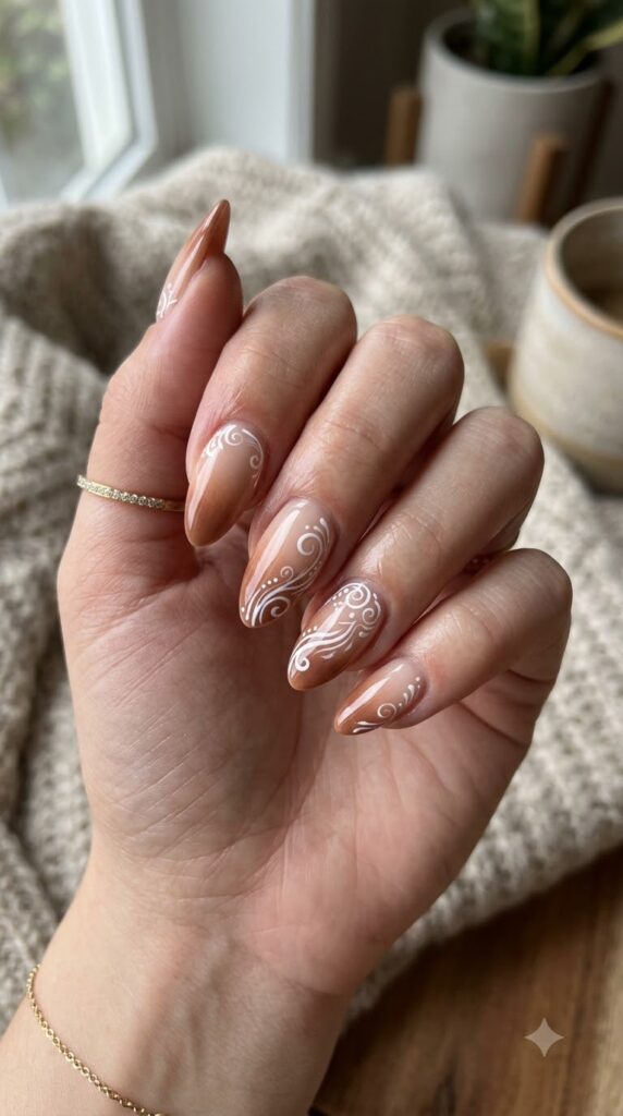 Almond nude base fading into cinnamon brown tips with white swirl art