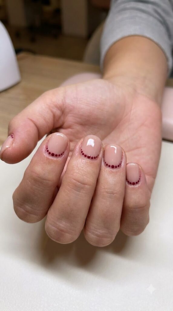 Short round blush nude nails bordered with tiny cranberry red dots