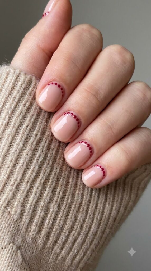 Short round blush nude gel nails bordered with tiny cranberry red dots