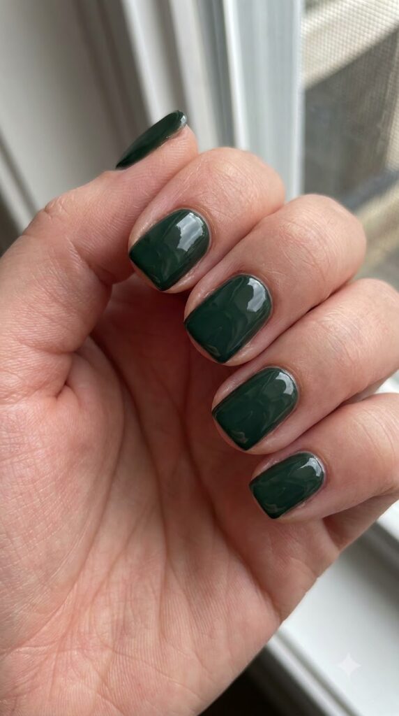 Short square nails painted in opaque dark forest green glossy polish