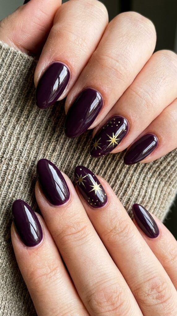 Almond glossy dark plum purple gel nails decorated with golden starbursts