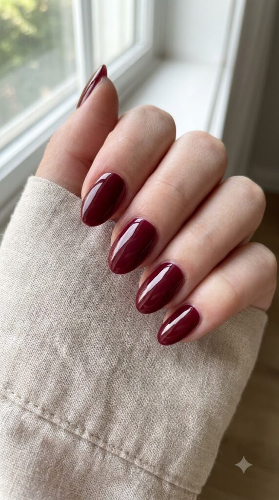 Short almond nails painted in classic deep dark red polish
