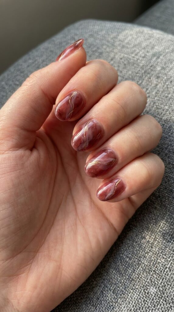 Short oval smoky red marble nails swirled with soft white and gold veins