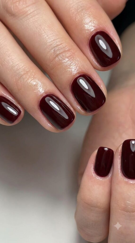 Short round nails painted in opaque deep oxblood red glossy polish