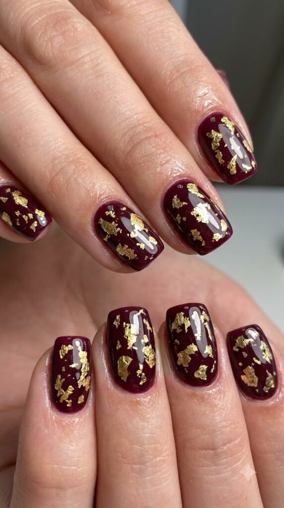 Short squoval burgundy nails decorated with torn gold foil flakes