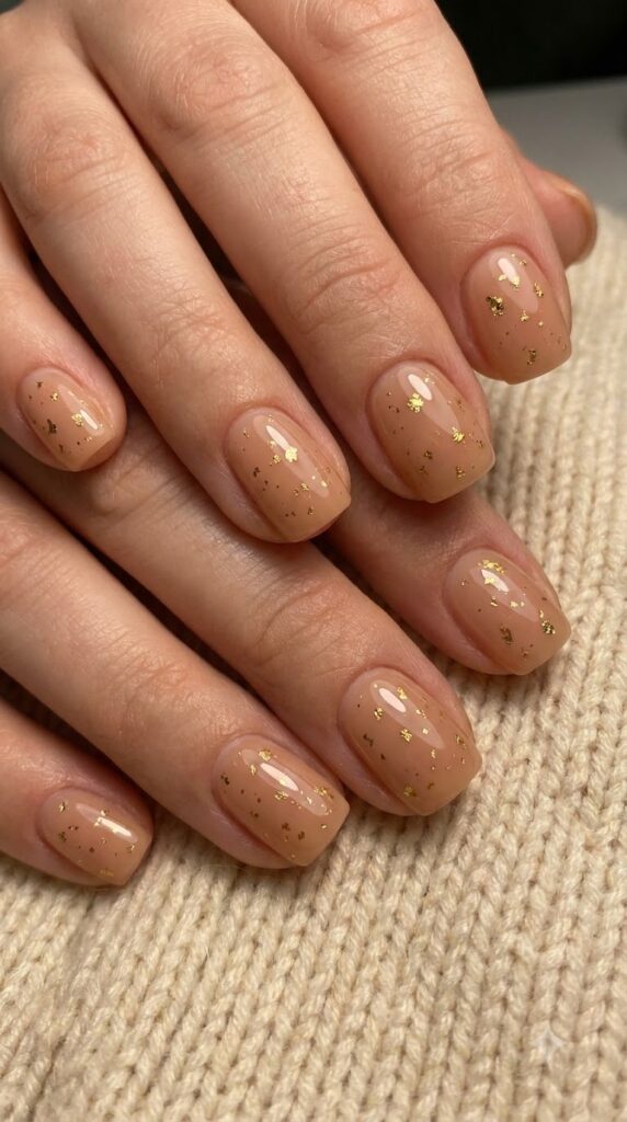 Short squoval nude nails decorated with delicate tiny gold foil flakes