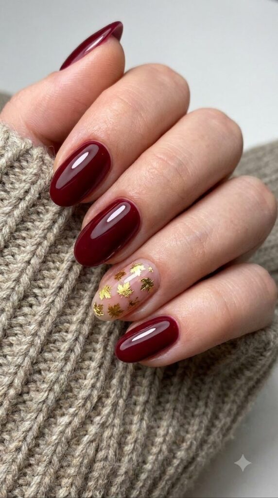 Oval dark burgundy red nails decorated with miniature gold foil maple leaves