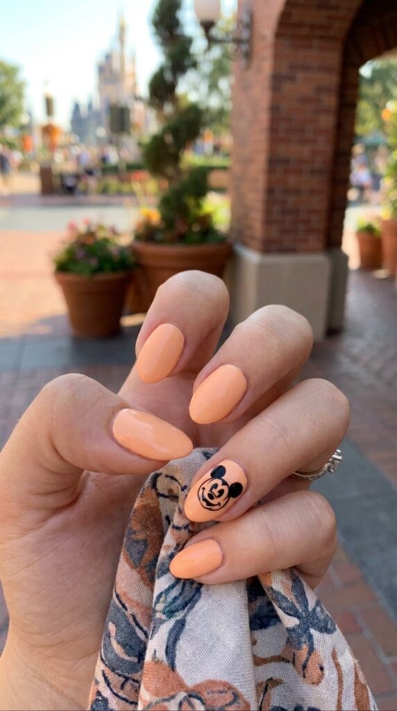 Short almond pastel orange nails with black Mickey pumpkin face art