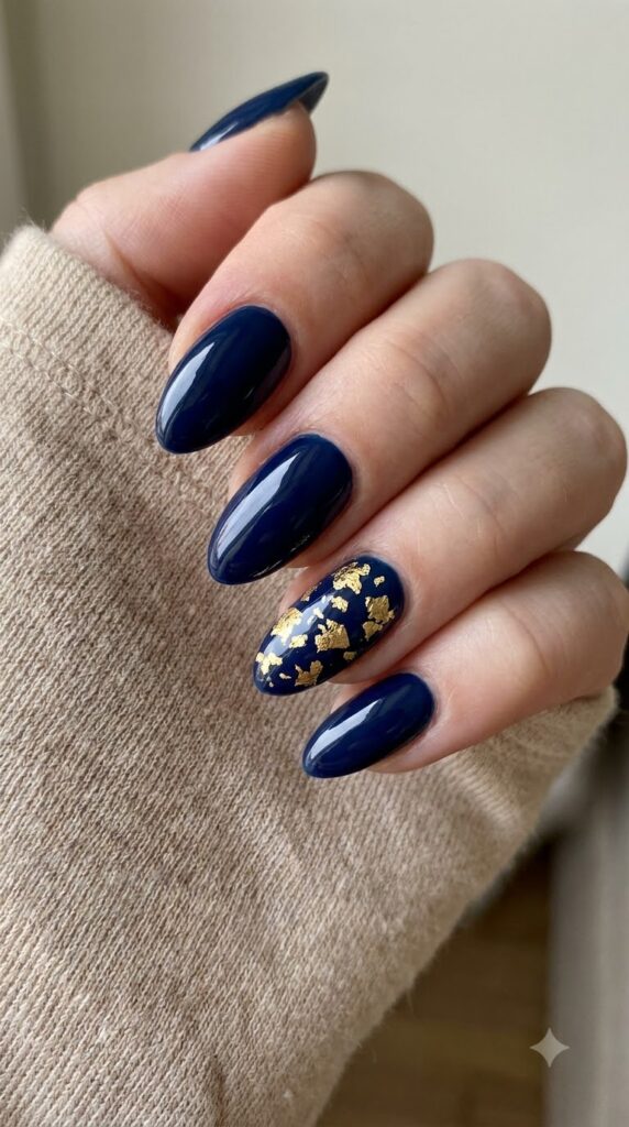 Medium almond nails with glossy midnight navy blue polish and gold leaf flecks
