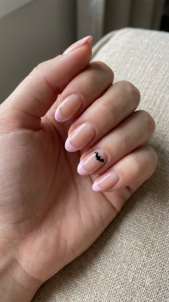 Short almond nude nails with pastel pink French tips and black bat accent