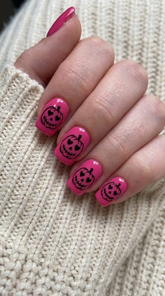 Short squoval hot pink nails with black carved jack-o-lantern smiles