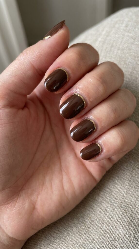 Short oval brown nails with thin metallic gold curves along the cuticles