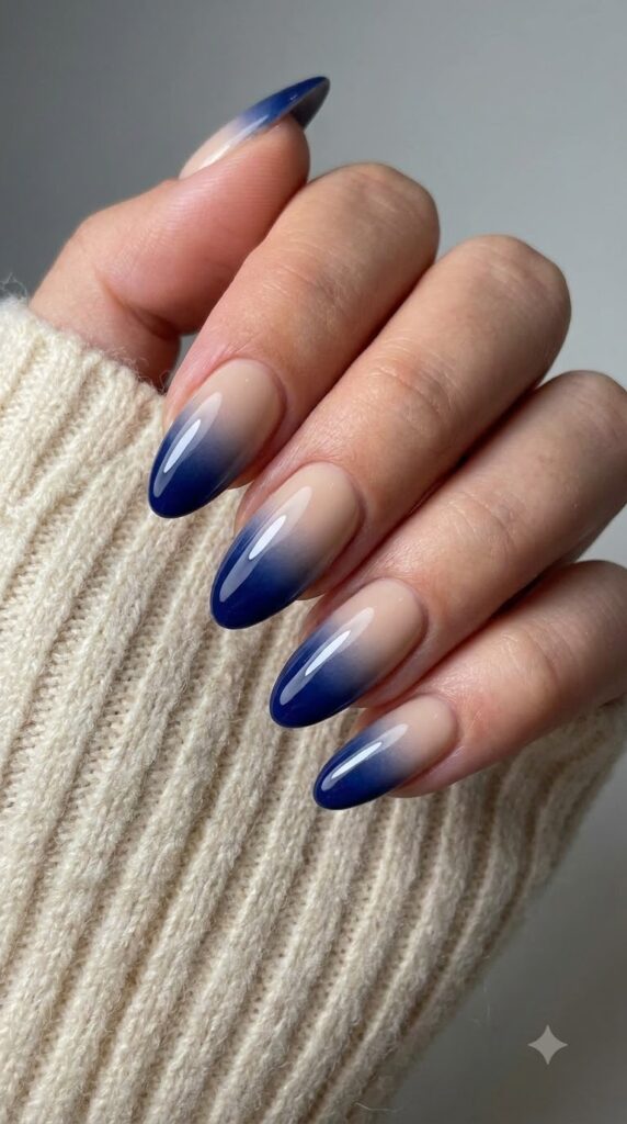 Medium almond nails with nude base fading smoothly into deep royal navy tips