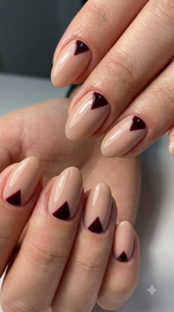 Short almond nude nails with dark burgundy triangle shapes at cuticles