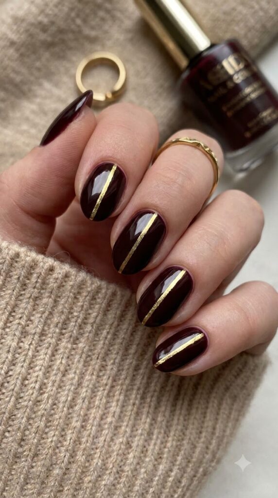 Short almond burgundy nails with a single thin vertical gold stripe
