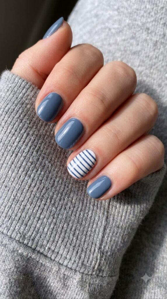 Short round dusty slate blue nails with a white and navy striped accent nail