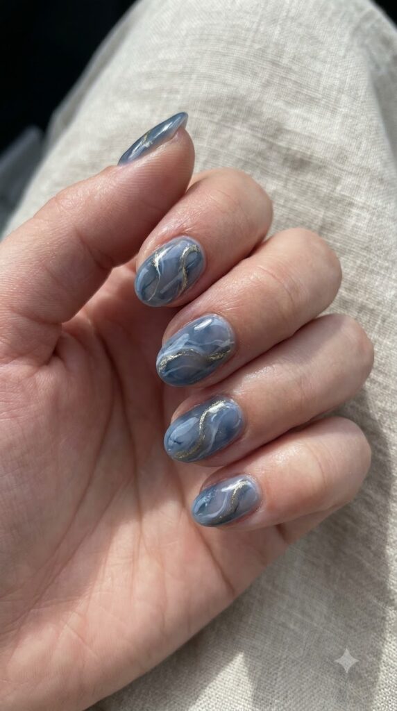Short oval smoky blue marble nails swirled with soft white and gold veins