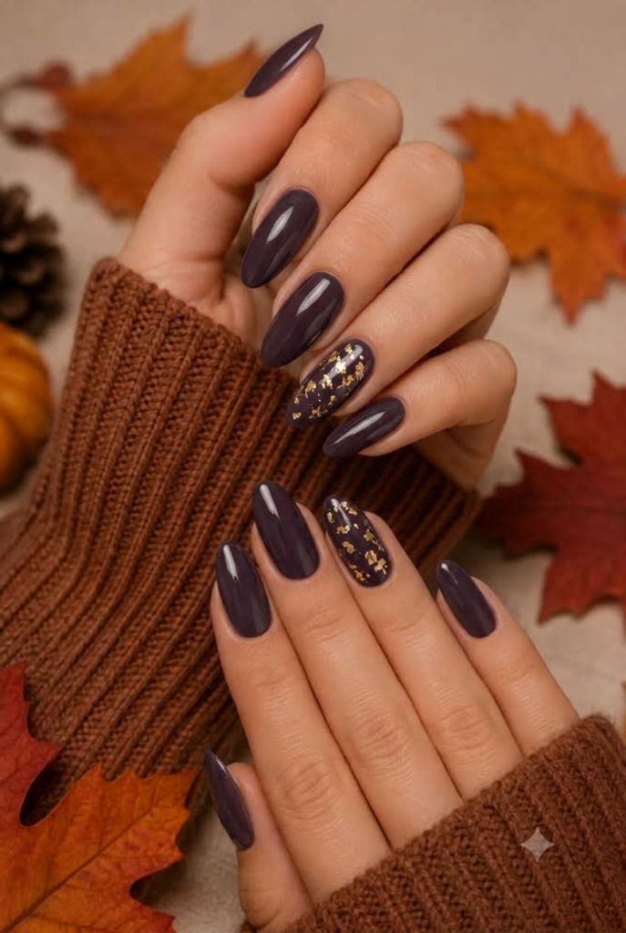 Almond deep smoky plum nails with scattered gold leaf foil on ring finger