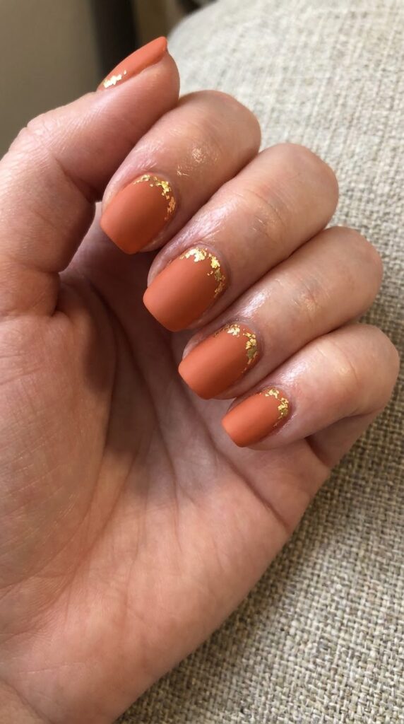 Short squoval terracotta orange nails decorated with gold leaf foil flecks