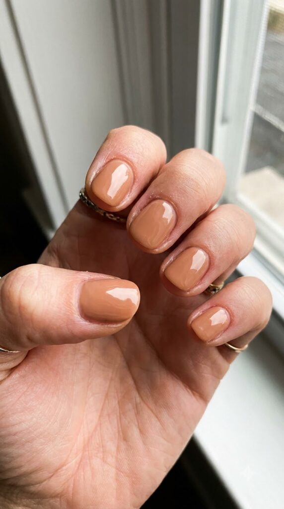 Short natural round nails painted in opaque warm toffee nude gel polish
