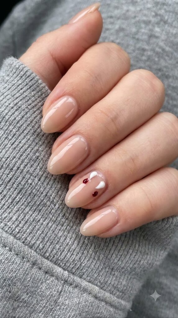 Short almond sheer nude nails with two tiny white vampire fang dots and blood