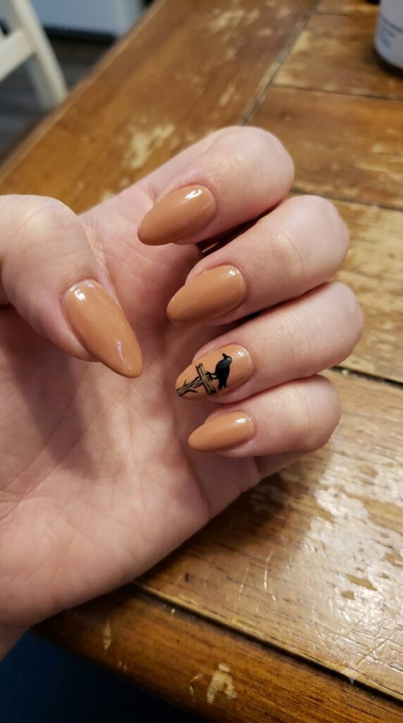 Medium almond caramel nude nails with a black crow perched on a scarecrow post