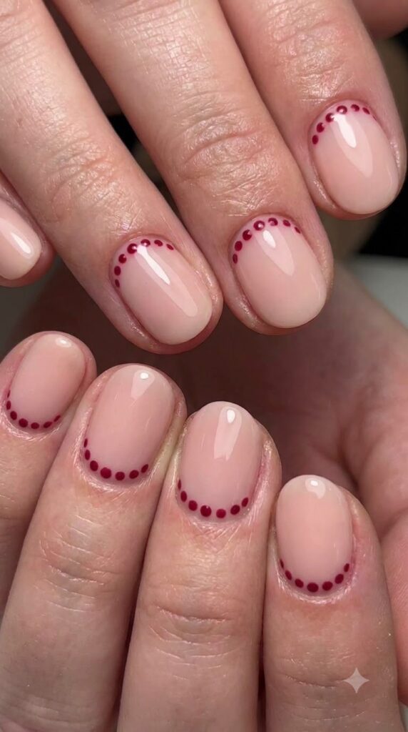 Short round blush nude nails bordered with tiny cranberry red dots