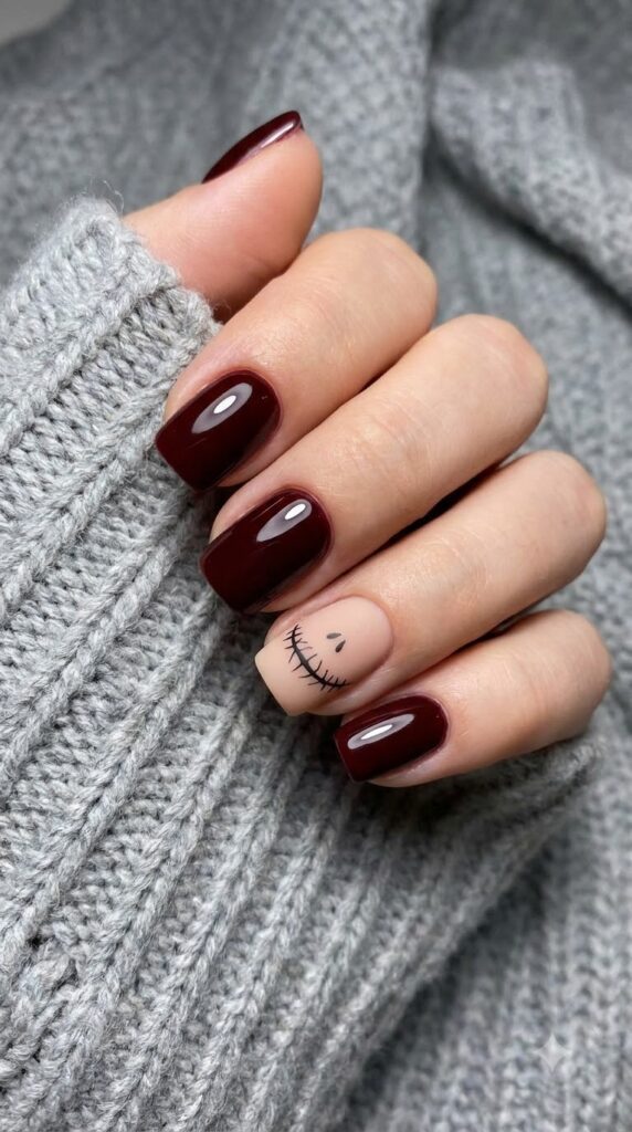 Short square burgundy nails with a nude accent nail featuring skeleton stitches