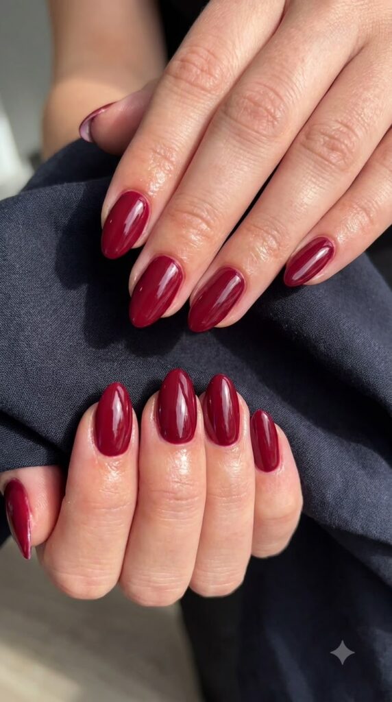 Short oval nails painted in opaque rich cranberry red glossy polish