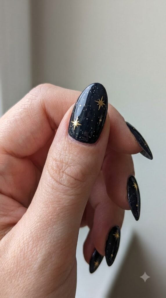 Almond black nails decorated with metallic gold starburst decals and glitter