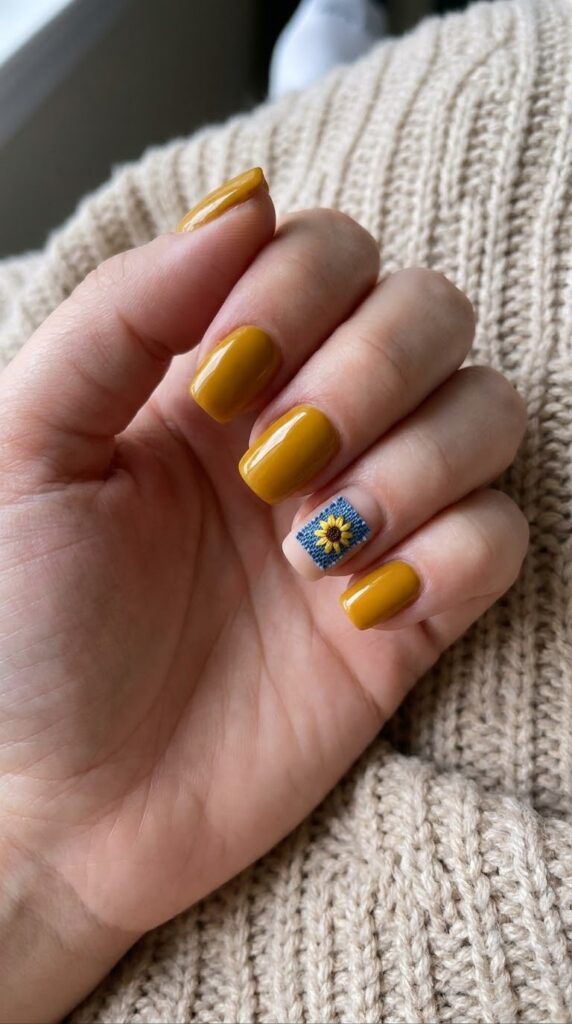 Short squoval mustard yellow nails with a blue fabric patch and sunflower art