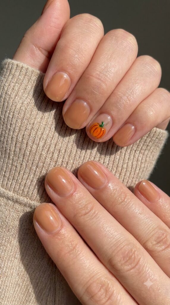 Short natural round caramel nude nails with a miniature painted orange pumpkin