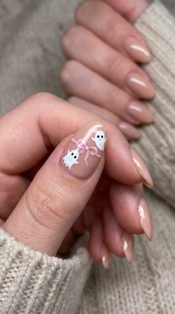 Short almond nude nails with tiny floating white ghosts tied with a pink ribbon bow