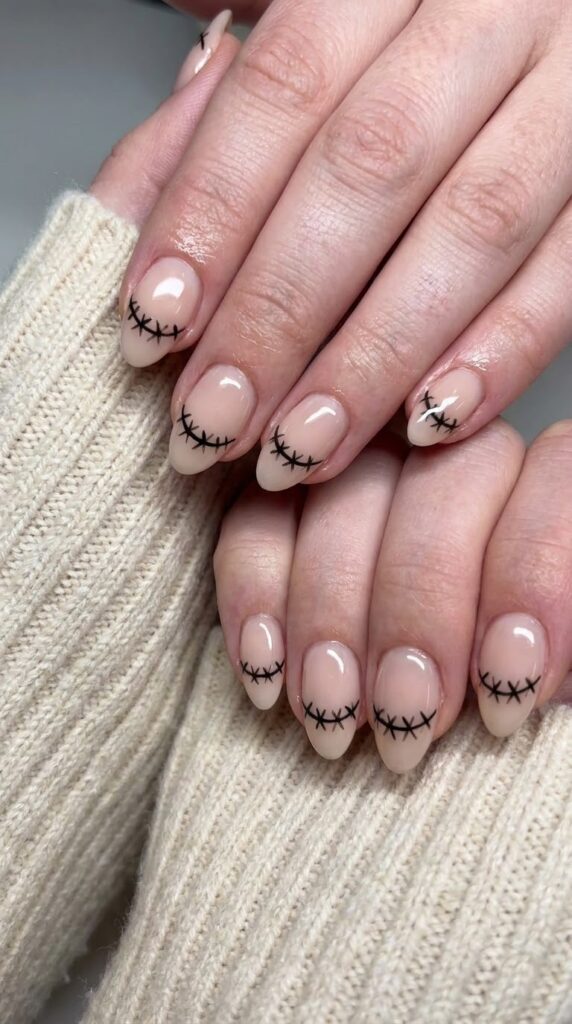 Short almond pale nude nails with a black stitched scarecrow mouth line