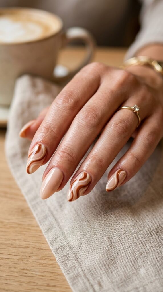 Almond nude nails decorated with flowing toasted cinnamon brown and cream swirls